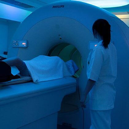 A woman in white shirt and pants near an mri machine.